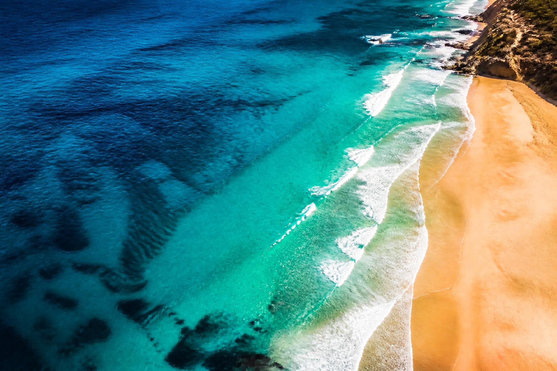 Aerial view of a coastline where deep blue and turquoise ocean water meets a sandy beach